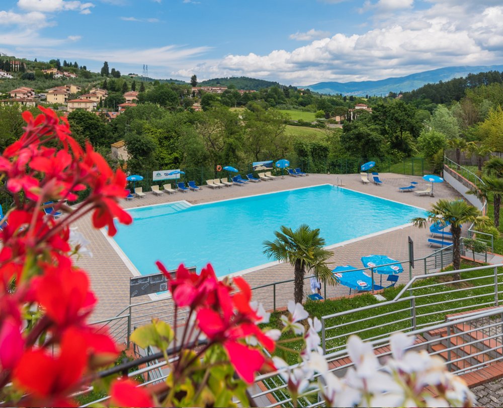 Piscina luminosa in collina, cielo azzurro e verde lussureggiante, atmosfera rilassante e serena.