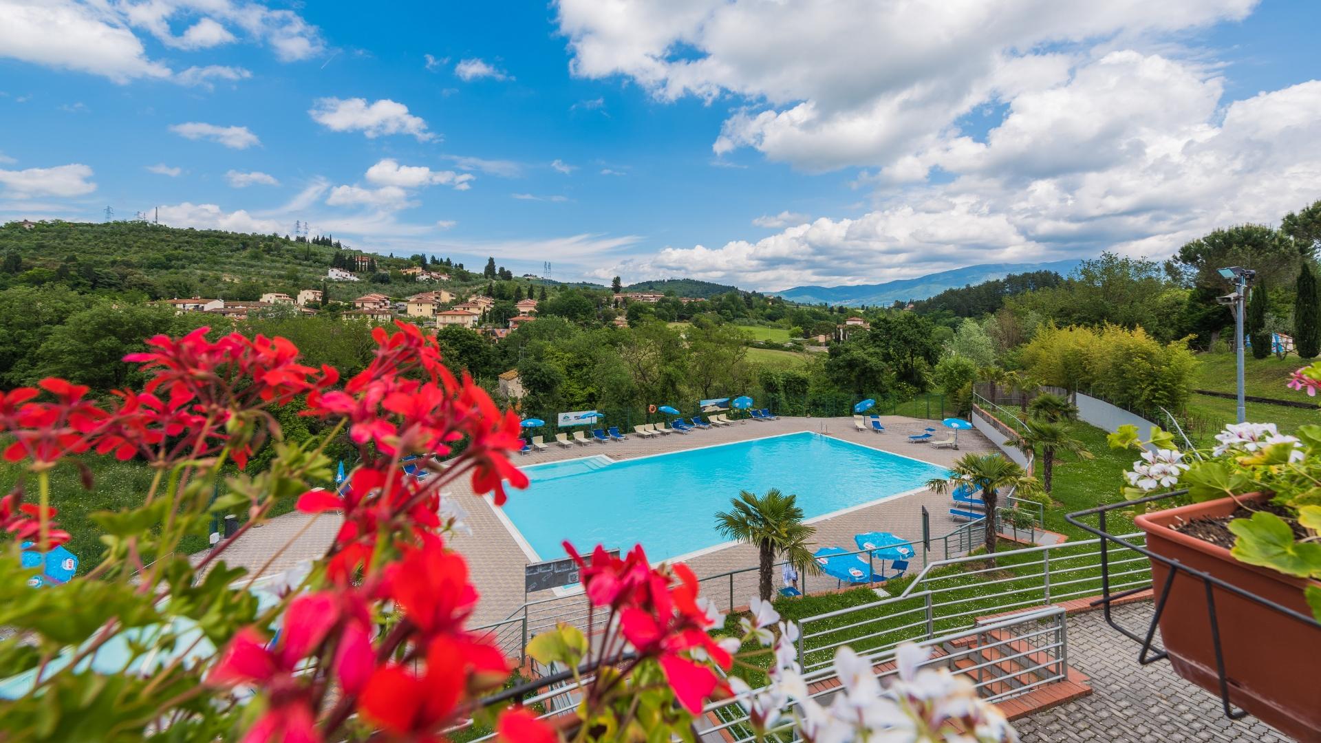 Piscina azzurra tra colline verdi, fiori vivaci e cielo sereno: un'oasi di tranquillità .