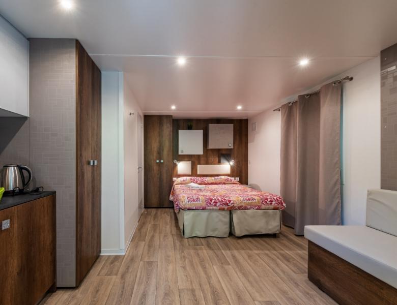 Accogliente camera moderna con letto colorato, angolo cucina e pavimento in legno elegante.
